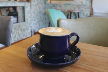 A blue coffee cup on the table, decorated with latte art in a lovely hipster cafe with interior decor in rustic style.