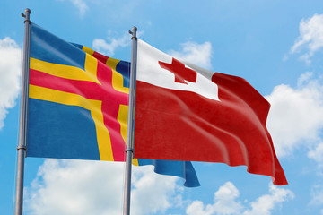 Tonga and Aland Islands flags waving in the wind against white cloudy blue sky together. Diplomacy concept, international relations.