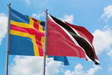 Trinidad And Tobago and Aland Islands flags waving in the wind against white cloudy blue sky...
