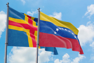 Venezuela and Aland Islands flags waving in the wind against white cloudy blue sky together. Diplomacy concept, international relations.