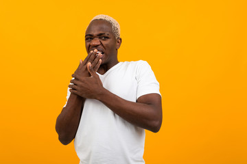 cute african blond guy in a white t-shirt yawns on a yellow isolated background