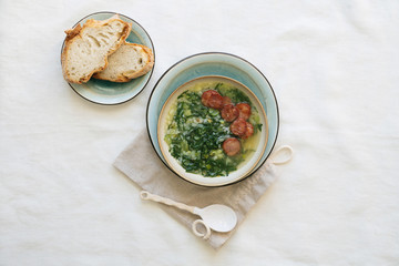 Caldo Verde Soup with greens and chopped chorizo on the top in ceramic bowl.