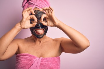 Middle age brunette woman wearing beauty black face mask over isolated pink background doing ok...