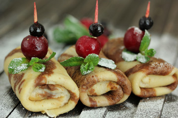 Concept of Russian cuisine. Chocolate pancakes on a dark wooden background with red berries and mint