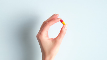 Woman hand holding pill or vitamin in capsule over blue background. Pharmacy and medicine concept