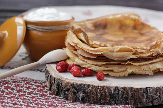 Concept of Russian cuisine. Pancakes with sour cream and strawberries on a wooden background. Copy space
