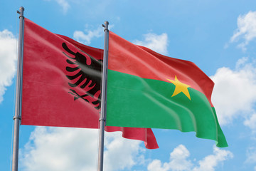 Burkina Faso and Albania flags waving in the wind against white cloudy blue sky together. Diplomacy concept, international relations.