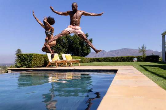 Young couple jumping on swimming pool on a sunny day