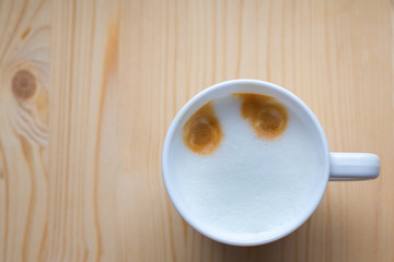 Beautiful white ceramic mug with tasty aromatic coffee and frothed milk stands on light wooden brown table, top view. Free space. Cooking in coffee machine. Coffee eyes, smiley face.