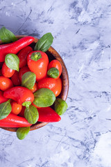 Red little bell peppers in a wooden plate on a gray background