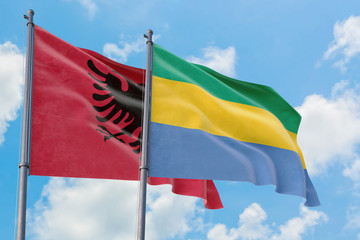 Gabon and Albania flags waving in the wind against white cloudy blue sky together. Diplomacy...