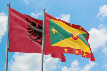 Grenada and Albania flags waving in the wind against white cloudy blue sky together. Diplomacy concept, international relations.
