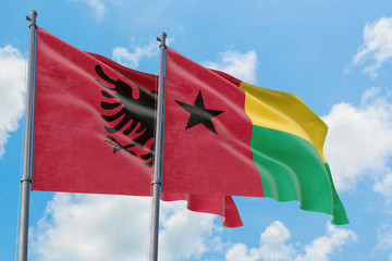 Guinea Bissau and Albania flags waving in the wind against white cloudy blue sky together. Diplomacy concept, international relations.