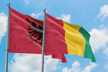 Guinea and Albania flags waving in the wind against white cloudy blue sky together. Diplomacy concept, international relations.