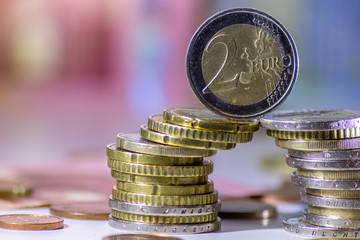 Stapel Euro-Münzen mit stehender 2-EURO-Münze aus 2 Euro, 1 Euro und Cent-Münzen mit einem Haufen Bargeld aus Geldscheinen und EURO-Münzen zeugt von Reichtum in der Finanzwelt und schnelles Geld