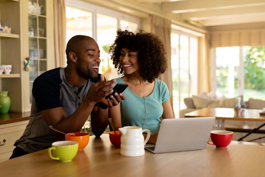 Happy Young Couple Using Computer And Mobile Phone In The Kitchen