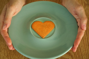 A heart shaped cookie on a plate in woomans hand.