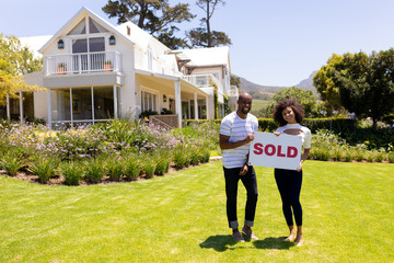 Happy young couple in the garden holding sold sign