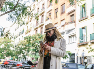 Attractive and elegant stylish blond caucasian woman looks smiling at her smartphone