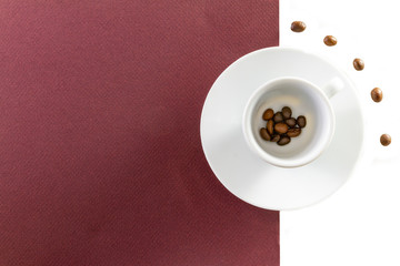 Top view of a coffee cup and coffee beans on brown and  white background