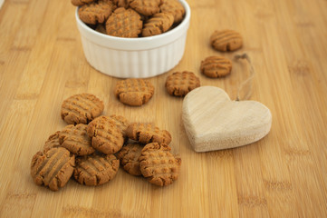 Very tasty peanut butter biscuits on bamboo wooden board in white baking bowl and decorative wood heart, golden baked healthy