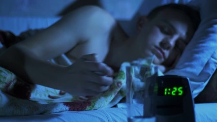 Anxious night and lack of sleep. A man drinks sedatives or sleeping pills at night in bed