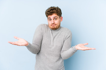 Young blond curly hair caucasian man isolated doubting and shrugging shoulders in questioning...