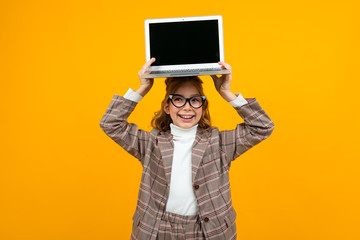 funny beautiful girl in a classic jacket holds a laptop with a mock up display forward on a yellow background with copy space