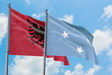 Micronesia and Albania flags waving in the wind against white cloudy blue sky together. Diplomacy concept, international relations.