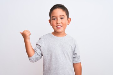 Beautiful kid boy wearing grey casual t-shirt standing over isolated white background smiling with happy face looking and pointing to the side with thumb up.