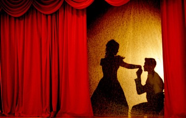 A man and woman in theatrical costumes in the theater of shadows on the stage with red curtains....