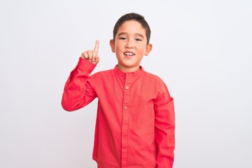 Beautiful kid boy wearing elegant red shirt standing over isolated white background showing and pointing up with finger number one while smiling confident and happy.