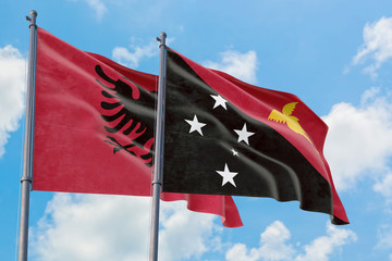 Papua New Guinea and Albania flags waving in the wind against white cloudy blue sky together. Diplomacy concept, international relations.