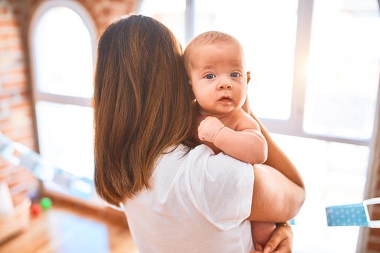 Young beautifull woman and her baby standing at home. Mother holding and hugging newborn