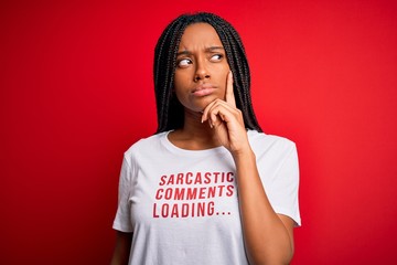 Young african american woman wearing sarcasm coments text on t-shirt over red background serious...