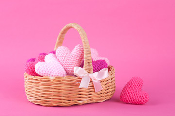Fototapeta na wymiar Wicker basket with multi-colored knitted hearts. Bright pink background. Festive decor. Valentine's Day. DIY