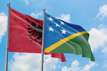Solomon Islands and Albania flags waving in the wind against white cloudy blue sky together. Diplomacy concept, international relations.