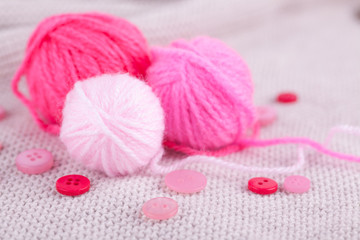 Obraz na płótnie Canvas Pink balls of yarn of different sizes and buttons on a gray knitted background. Handicraft, needlework, hobby, knitting, DIY