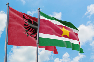 Suriname and Albania flags waving in the wind against white cloudy blue sky together. Diplomacy concept, international relations.