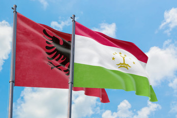 Tajikistan and Albania flags waving in the wind against white cloudy blue sky together. Diplomacy concept, international relations.