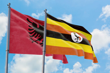 Uganda and Albania flags waving in the wind against white cloudy blue sky together. Diplomacy concept, international relations.