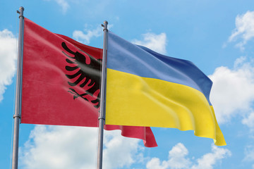 Ukraine and Albania flags waving in the wind against white cloudy blue sky together. Diplomacy concept, international relations.