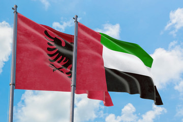 United Arab Emirates and Albania flags waving in the wind against white cloudy blue sky together. Diplomacy concept, international relations.