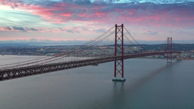 The Bridge of 25th April with car traffic and panoramic view of the city on the background after sunset, Lisbon, Portugal, 4k