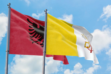 Vatican City and Albania flags waving in the wind against white cloudy blue sky together. Diplomacy concept, international relations.