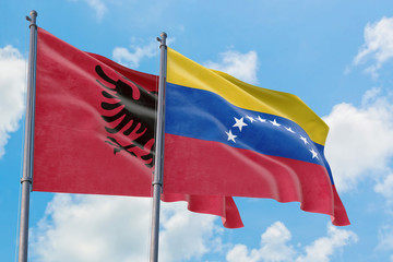 Venezuela and Albania flags waving in the wind against white cloudy blue sky together. Diplomacy...