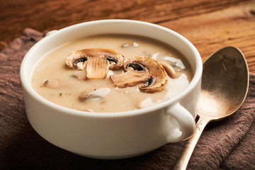 Closeup white bowl of mushroom soup with spoon and napkin on a wooden table