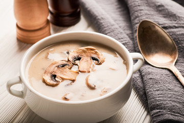 White bowl of mushroom soup and a napkin with a spoon on a wooden background