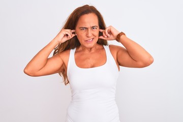 Middle age mature woman standing over white isolated background covering ears with fingers with annoyed expression for the noise of loud music. Deaf concept.
