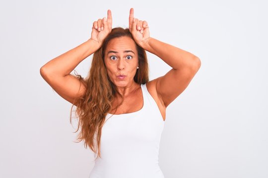 Middle age mature woman standing over white isolated background doing funny gesture with finger over head as bull horns
